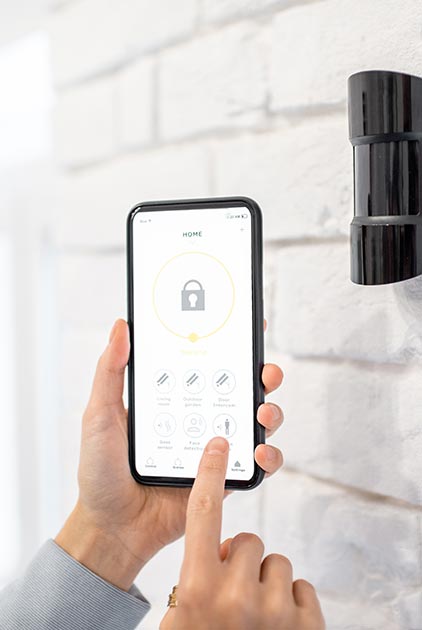 main tenant un smartphone à proximité d'une alarme fixée sur un mur